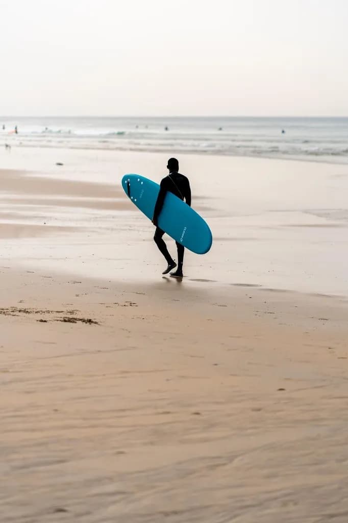 Surfer walking along Taghazout beach with a surfboard